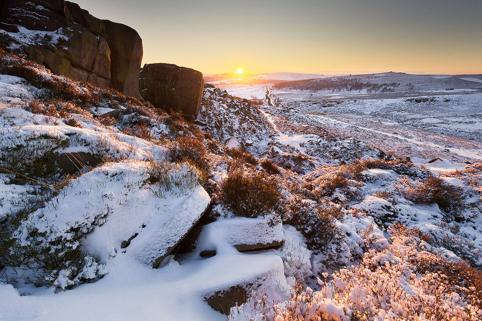 Burbage Edge Millstones in Snow. After sunrise one morning on Over Owler Tor I decided to spend the whole day out in the snow, finishing with sunset at Burbage Edge. I've photographed these abandoned millstones many times over the years but never before with a coating of snow. When I arrived I was pleasantly surprised to find that no one else had passed by yet and the snow was still nice and fresh! In contrast to the overcast morning there wasn't a cloud in the sky and the sun created a beautiful warm glow as it dipped below the horizon.