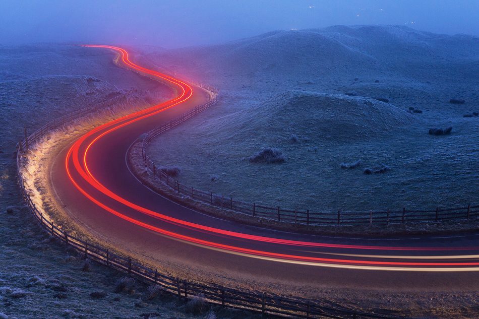 Light trails at the famous winding Mam Nick road below Mam Tor. Temperature: -5 with freezing fog. Derbyshire, Peak District National Park. This is an image I’ve had in mind for a long time now but have been waiting for the right conditions. It was absolutely freezing sat waiting for the cars to come by, every blade of grass was covered in thick frost and I could barely see anything in the thickest patches of drifting fog. Everything came together in the end though, and after capturing a few light trails I headed back home to the warmth. ABOUT MAM TOR: Mam Tor is a 517m hill near Castleton, in the High Peak area of the Peak District National Park. The hill gets its nickname ‘The Shivering Mountain’ from the frequent landslips that occur on the eastern face of the hill, caused by unstable layers of shale. At the base of Mam Tor and at nearby Winnats Pass are four famous caverns where semi precious minerals such as Blue John were once mined. These caverns are known as; the Blue John Cavern, the Peak Cavern, the Speedwell Cavern, and the Treak Cliff Cavern.