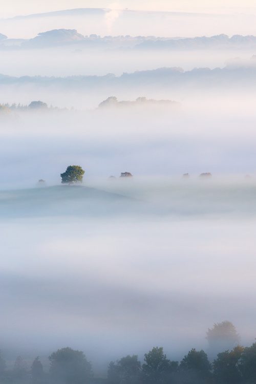 Misty morning view from above Earl Sterndale, a tiny village in the White Peak, looking over the valley with features in the landscape starting to emerge from under the waves of thick fog. Taken on an Autumnal misty Peak District morning.